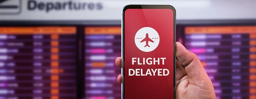 Modern technology in travel Concept. Flight Delayed on Smartphone Screen. Businessman using Mobile Phone in front of Departures Board to Re-Checked Flight Information in Airport. Claim flight delay compensation.