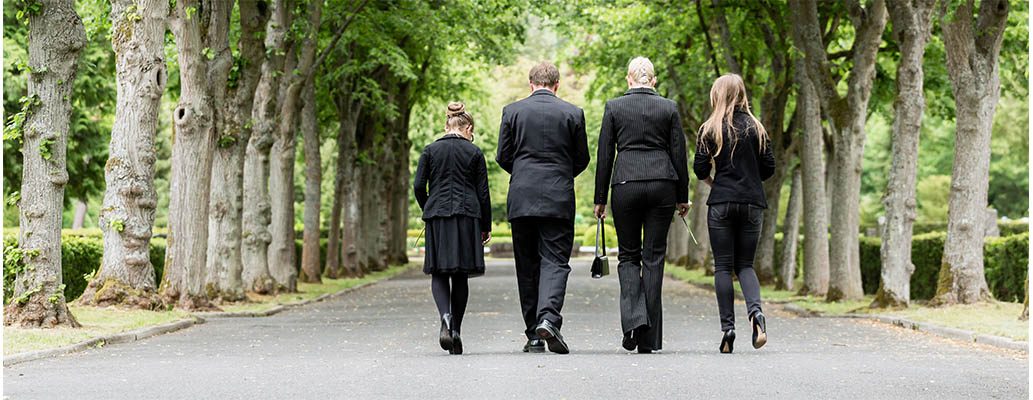A group walk away from a funeral, dressed in black.