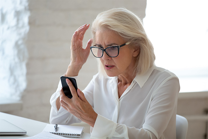 A woman with grey hair looking confusedly at her phone.
