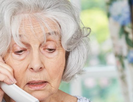 A woman with grey hair looking upset on a phone