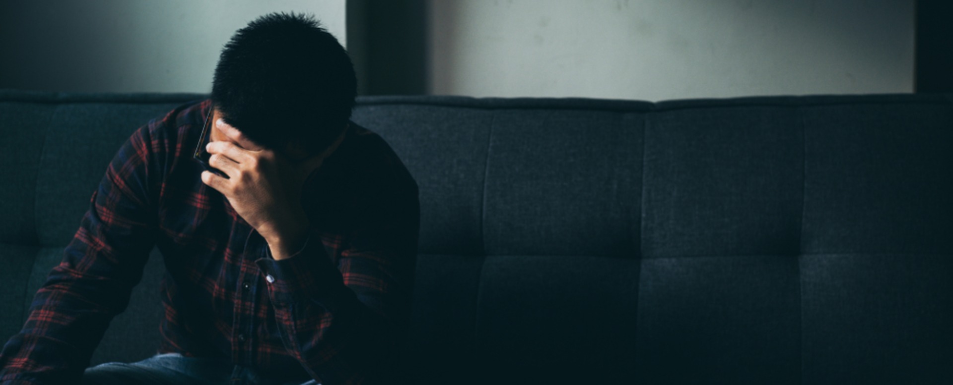 An abused man sits on a sofa with his heads in his hands