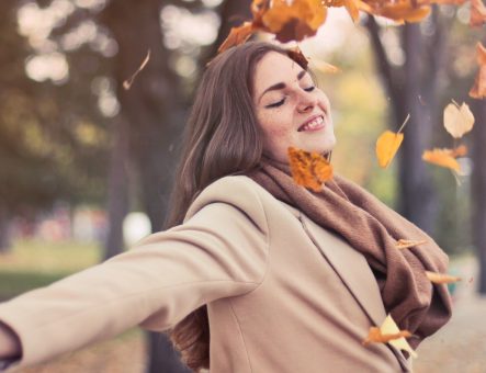 A woman looking happy and free as Autumn leaves fall around her.