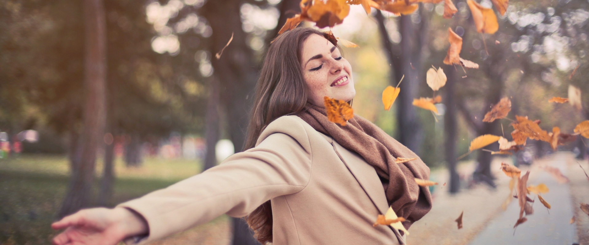 A woman looking happy and free as Autumn leaves fall around her.