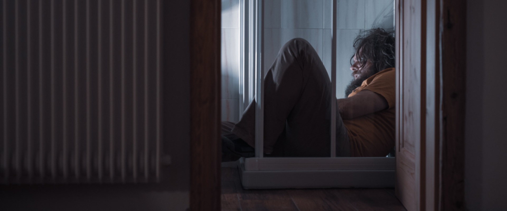 A man hiding on the floor of a shower depressed