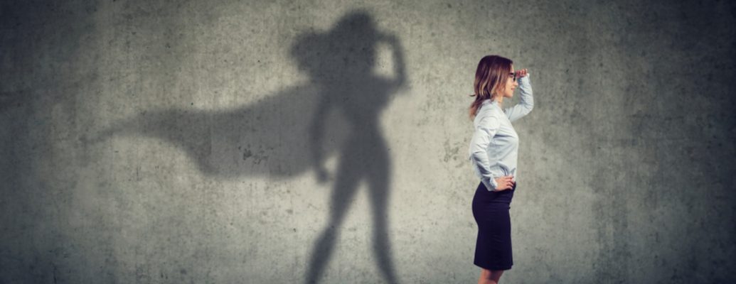 A woman stands looking into the future whilst her shadow depicts superwoman