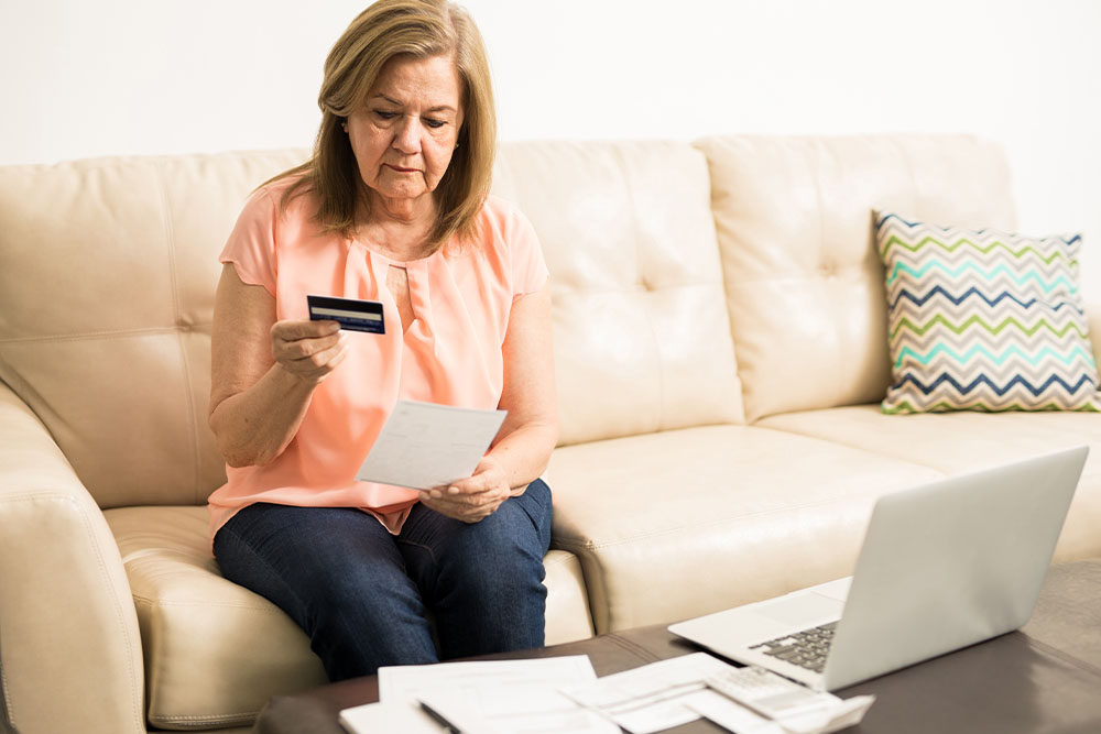 A woman sits on her sofa looking sadly at a credit card