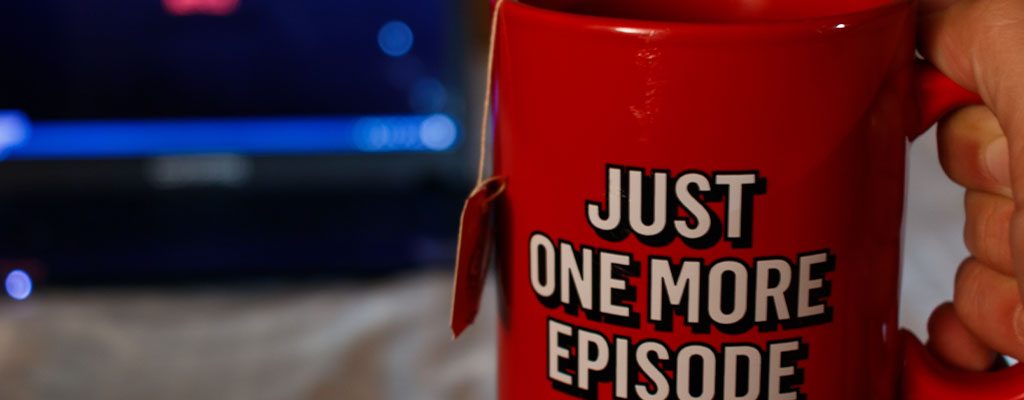 A mug which says 'Just one more episode' in front of a TV.