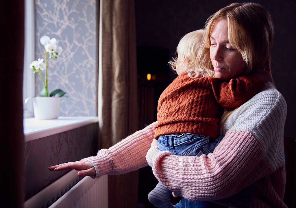A woman holds her child close as she checks to see if the heating is on.