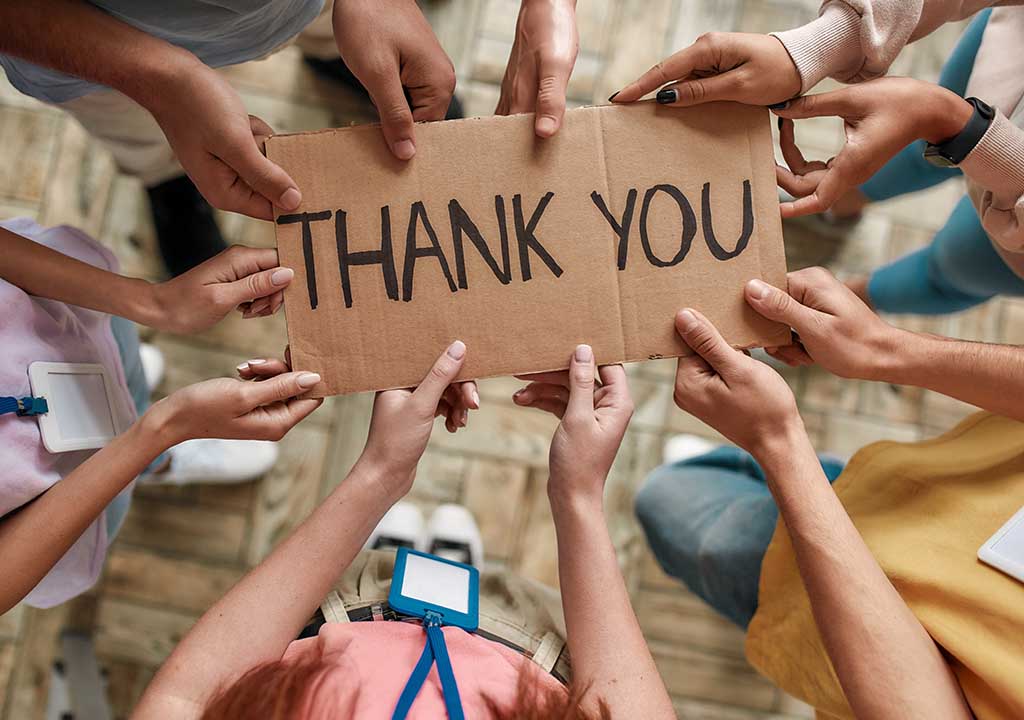 Hands holding a hand written thank you sign.