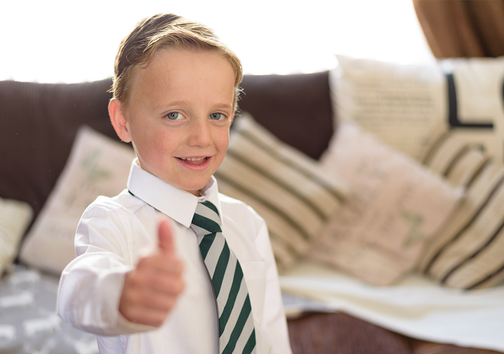 A boy in school uniform giving a thumbs up.