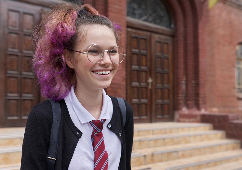 A girl with pink hair in school uniform smiling.